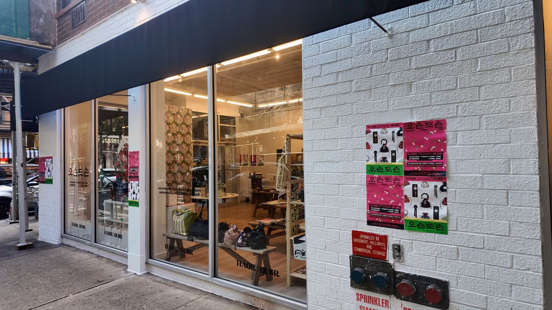 The HAOR x OUWR pop-up storefront at 21 Spring Street, with Oson Doson posters on the white brick wall and bags on a bench visible through the windows
