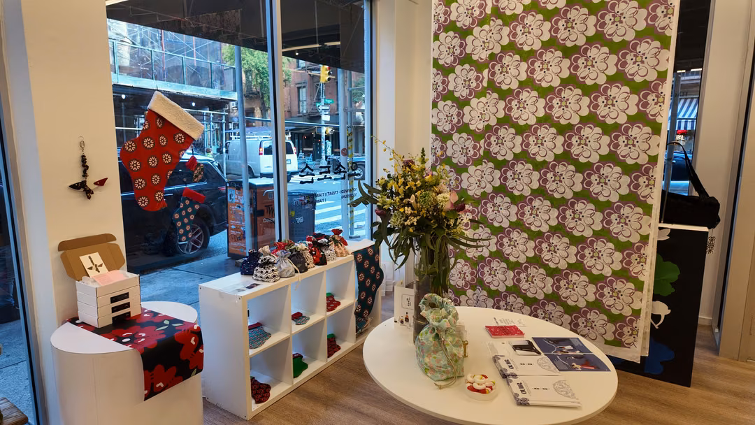 A corner by the front window of the pop-up: a red patterned stocking hanging in the glass, a white shelf of hats and socks, and a large green and purple floral fabric panel