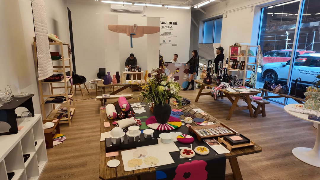 Wide view of the HAOR x OUWR shop: a long wooden table of cushions, tableware and accessories in the foreground, with shelving and a hanbok jacket on the back wall